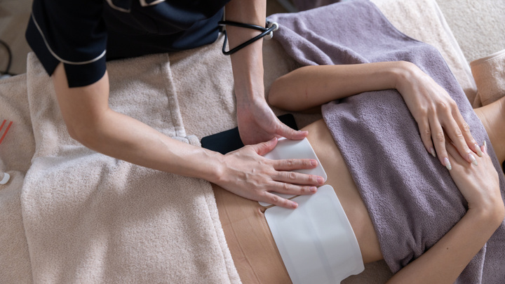 承認済み実写素材を使用した、お腹にシート状電極を貼付する施術風景